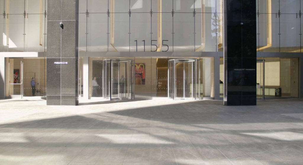Modern commercial building entrance with revolving doors and large glass façade, showcasing the address "1155" prominently, relevant for real estate marketing and visibility strategies.