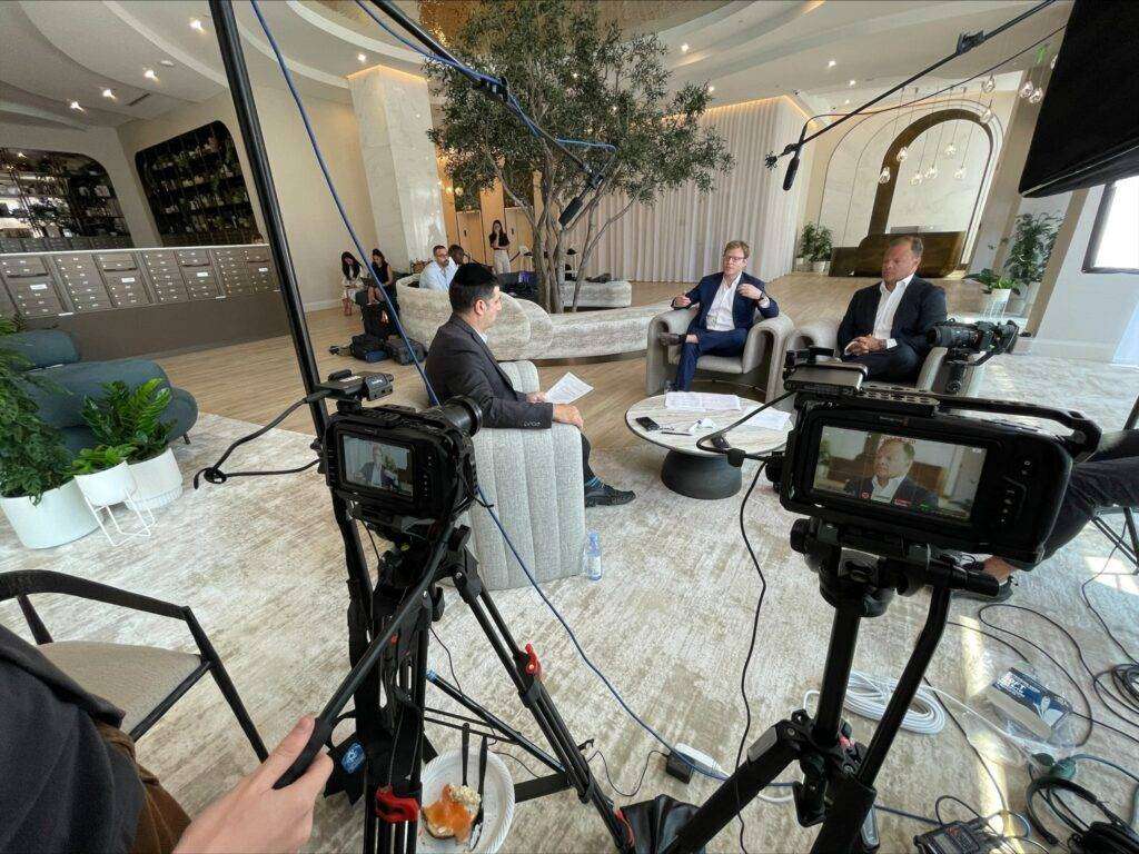Two men seated in modern chairs discussing video marketing strategies, with cameras and microphones set up for a professional interview in a stylish, well-lit interior space.
